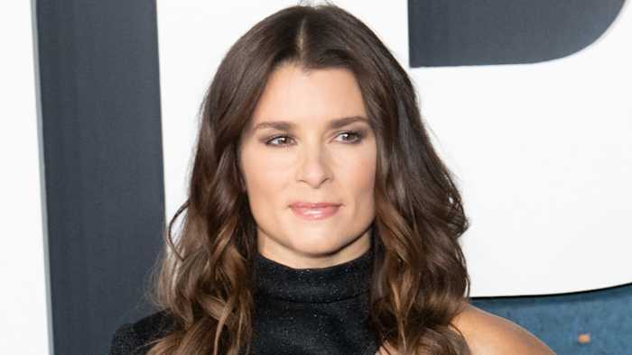 Danica Patrick poses in a black high-neck dress and looks off to the side of the camera.